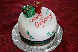 A Christmas Cake for Boxing Day. A white Christmas cake with two mini present boxes, a tarten ribbon, and the words "Merry Christmas"