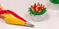 A pastry bag fitted with a leaf tip is used to decorate a cupcake