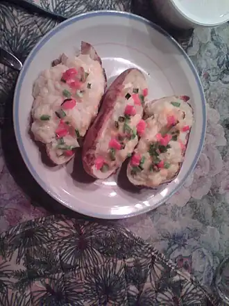 Three twice-baked potatoes, with green onions and red bell peppers on top, on a plate ready to serve.