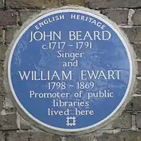 A Blue plaque on a brick wall with the words "John Beard C1717&nbsp;– 1791 Singer and William Ewart 1798&nbsp;– 1861 Promoter of Public Libraries