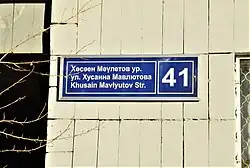 Современный трёхъязычный вариант адресной таблички: ул. Мавлютова, 41 – используется ненормативное написание фамилии на татарском языке (ноябрь 2018)
