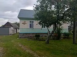 Дом с покатой крышей. Перед домом - дерево. Слева на заднем плане - дворовые постройки.