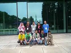 Десять человек стоят лицом вперед, в две шеренги по пять человек. В первом ряду сидят пятеро подростков. За ними — пятеро взрослых.