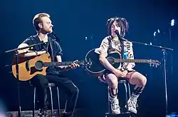Billie Eilish and Finneas O’Connell, holding their acoustic guitars