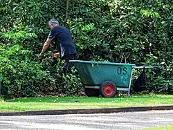 садовник в Великобритании с большой тачкой