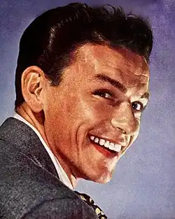 Close-up studio photograph of a young, smiling Sinatra with styled hair wearing a suit and tie