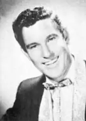 A dark-haired man in a tuxedo, smiling broadly