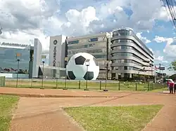 У входа в музей установлен огромный футбольный мяч; на заднем плане — гостиница «Bourbon Asunción»