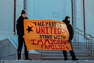 Два протестующих держат проиммигрантский плакат на протесте в день инаугурации Дональда Трампа в Берлингтоне