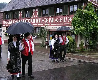 Жители в народных костюмах, на заднем плане — дом XVIII в.