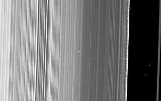 S/2009 S1 виден в центре как яркая точка с длинной тенью. Справа видна щель Кассини