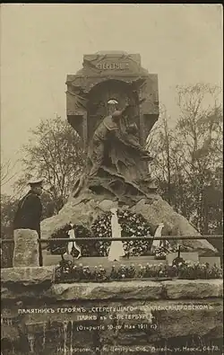 Фотооткрытка с видом на скульптурную часть монумента «Стерегущему». На площадке у монумента, слева, стоит мужчина в форменной одежде и фуражке. У подножия памятника венки с лентами, у края верхней площадки высажены тюльпаны.