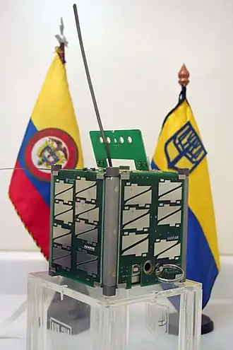 Спутник Libertad 1 на выставке, на фоне — флаги Колумбии и университета