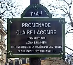 Табличка на столбе с надписью: 11 e Ar t — PROMENADE CLAIRE LACOMBE — 1765 – APRĖS 1798 — ACTRICE, FÉMINISTE, CO-FONDATRICE DE LA SOCIÉTÉ DES CITOYENNES RÉPUBLICAINS RÉVOLUTIONNAIRES