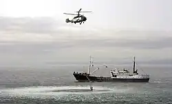 Отработка поисково-спасательных действий экипажем вертолёта Ка-27ПС авиации ФСБ России — подъём из воды «пострадавшего» в ходе российско-японских учений пограничных служб в заливе Анива.На заднем плане: условно-пиратское судно-нарушитель с «Весёлым Роджером» на борту — пограничное патрульное судно ОМБИР Береговой охраны ПС ФСБ России «Афалина» проекта 502Р (2009 год).