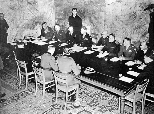 Подписание капитуляции в Реймсе.Спиной: Ганс Фридебург, Альфред Йодль, Вильгельм Оксениус. В центре, слева от свободного стула — Уолтер Беделл Смит, справа — Иван Суслопаров