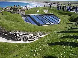 Вид с воздуха на поселение; здание 7 покрыто защитной плёнкой. На заднем плане видно современное побережье