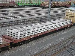 Платформа дороги VR, гружёная шпалами. Позади видны платформы-лесовозы