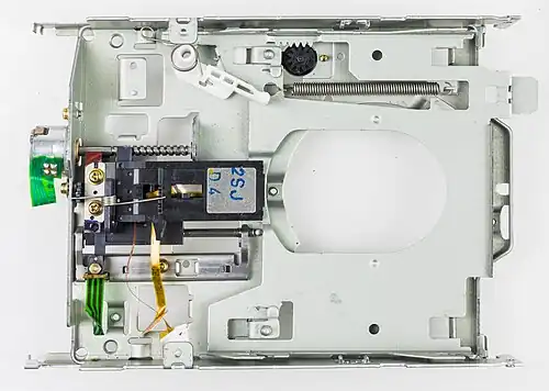 Вид без платы управления, двигателя и верхней части загрузочной рамки, но с шаговым двигателем и головками. Рычаг открытия створки виден полностью, также видны два контрольных штифта, не дающие вставить дискету не той стороной.