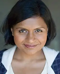 A close-up of Mindy Kaling's face. Kaling smiles into the camera. Her hair is shorter than shoulder-length; it is parted on the left, and swept back behind her right ear.